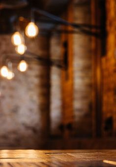 an empty wooden table with some light bulbs hanging from the ceiling in front of it