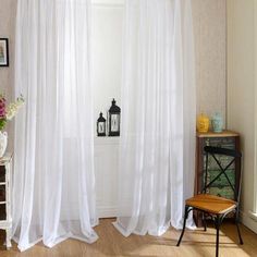 a white curtain hanging in front of a window next to a table with flowers on it