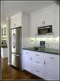 a stainless steel refrigerator and microwave in a kitchen with white cabinets, wood flooring and hardwood floors