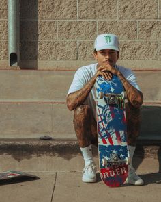 a man sitting on the ground with his skateboard in front of him, holding his hands to his face