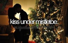 a man standing next to a christmas tree with the words kiss under mistetoe