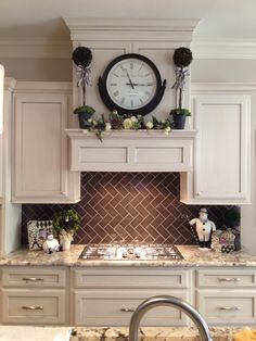 a clock mounted on the wall above a stove top in a kitchen with white cabinets