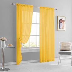 a yellow curtain hanging in front of a window next to a white chair and table