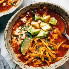 two bowls of mexican soup with tortilla noodles and avocado on the side