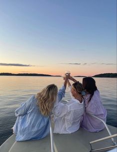 two women sitting on the back of a boat toasting with each other while looking out over water