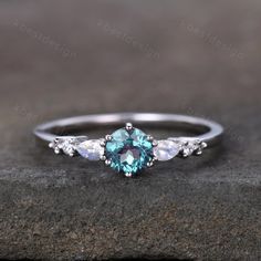 a blue and white diamond ring with three pear shaped diamonds on the side, sitting on top of a rock