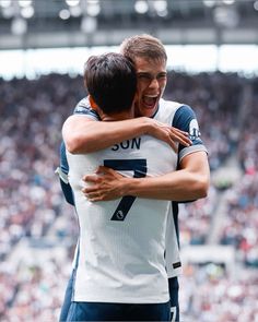 two soccer players hugging each other in front of a stadium full of people with their arms around one another