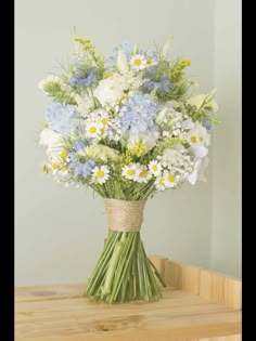 a bouquet of blue and white flowers in a vase on a wooden table next to a wall