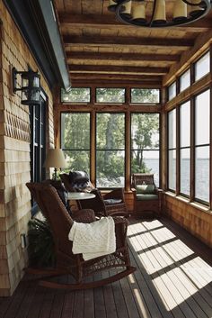 a porch with rocking chairs and windows overlooking the water is shown in this photo from inside