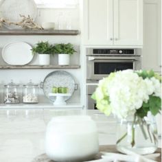 a kitchen with white cabinets and open shelving above the countertop is filled with flowers