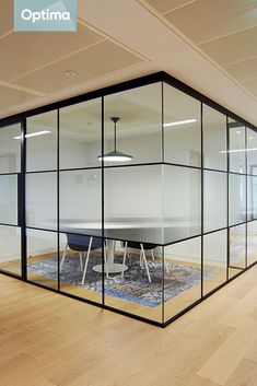 an office meeting room with glass walls and wooden flooring is seen from across the room