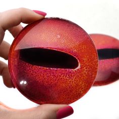 two red balls with black holes in them being held by someone's hand on a white surface