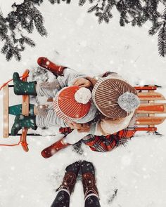 two people sitting on a sleigh in the snow with their feet up and hats down