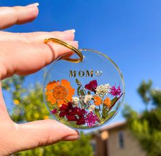 a hand holding a clear glass ornament with flowers on it that says mom