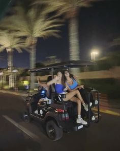 two girls riding in a golf cart on the street at night with palm trees behind them