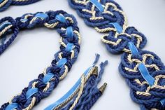 blue and gold braided necklaces are laying on a white surface with one knot in the middle