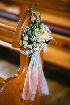 a bouquet of flowers sitting on the back of a wooden church pew with ribbon around it