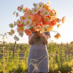 a woman holding a bouquet of flowers in front of her face with the sun behind her