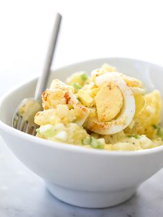 a white bowl filled with food on top of a table next to a fork and knife