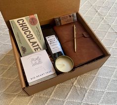 an open box containing chocolate and other items on a bed with a pen in it