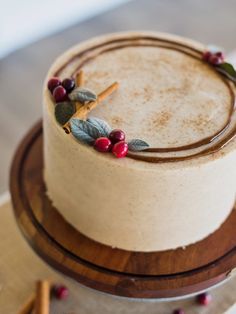 a close up of a cake with berries and leaves on the frosting, sitting on top of a wooden platter