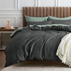 a bed with grey and green comforters in a white room next to a brown headboard