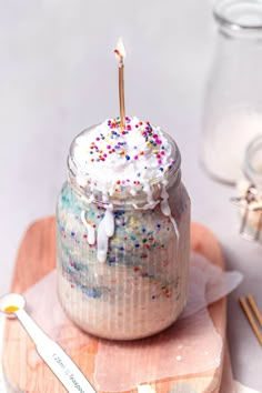 a birthday cake in a jar with sprinkles and a candle on top