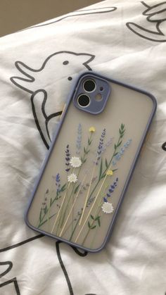 a phone case with flowers painted on it sitting on top of a white bed sheet