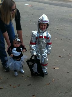 a young child dressed in an astronaut suit standing next to a woman and holding a baby doll