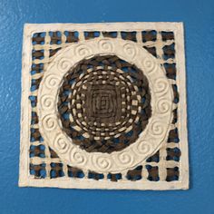 a white and brown wall hanging on the side of a blue wall with an intricate design