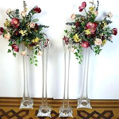 two tall vases with flowers in them sitting on a floor next to each other