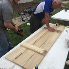 two men are working on wood planks in the yard with one man holding a drill