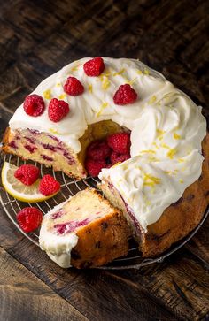 a cake with white frosting, raspberries and lemon slices on a wire rack