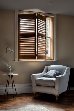 a white chair sitting in front of a window with wooden blinds on it's side