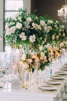 an elegant table setting with candles, flowers and greenery on the centerpieces