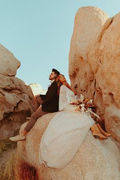 a man and woman sitting on top of a rock in front of large rocks with flowers