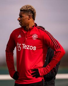 a man standing with his hands on his hips wearing a red shirt and black pants