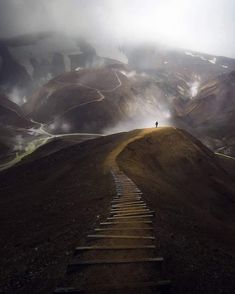 a person standing on top of a hill next to a set of stairs with clouds in the background