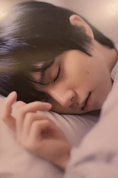 a woman sleeping on top of a bed next to a white pillow with her eyes closed