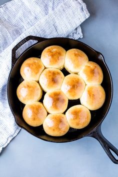 a cast iron skillet filled with rolls on top of a blue tablecloth next to a white towel