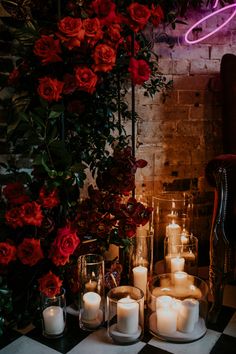 candles and roses on a table in front of a brick wall with a neon sign