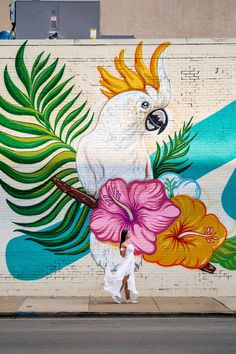 a large white parrot painted on the side of a building next to a woman walking past it