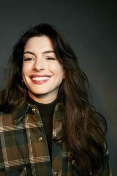 a woman with long dark hair smiling at the camera and wearing a green plaid coat