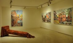 an art gallery with paintings on the wall and floor in front of two large wooden logs