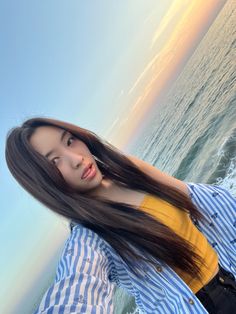 a woman with long hair standing by the ocean