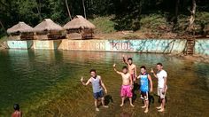 four men standing in shallow water with their arms up and one man waving to the camera