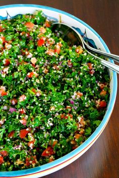 a bowl filled with salad on top of a wooden table next to a metal spoon