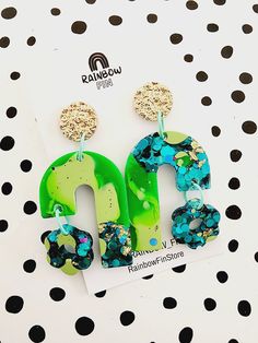 a pair of green and blue earrings sitting on top of a polka dot table