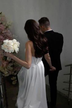 a woman in a white dress holding a bouquet of flowers next to a man in a tuxedo