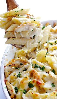 a wooden spoon scooping pasta from a casserole dish with chicken and parmesan cheese